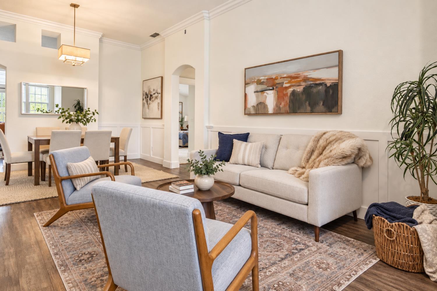 Warm living room with a cream sofa, wood-framed chairs, and abstract artwork